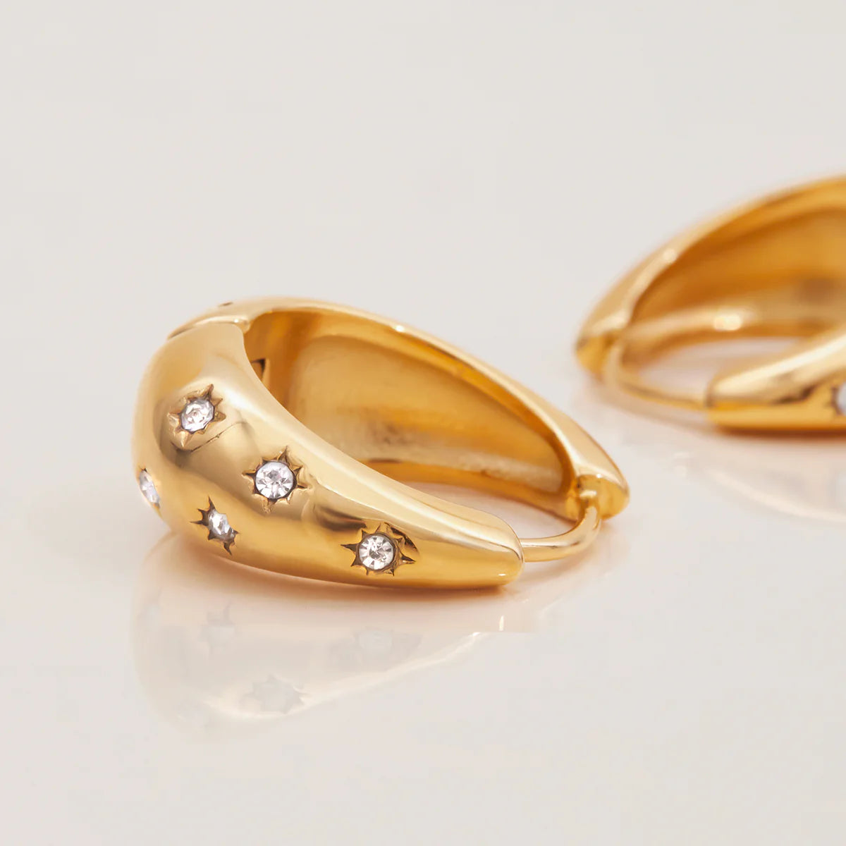 Gold hoop earrings with embedded diamonds on a light background