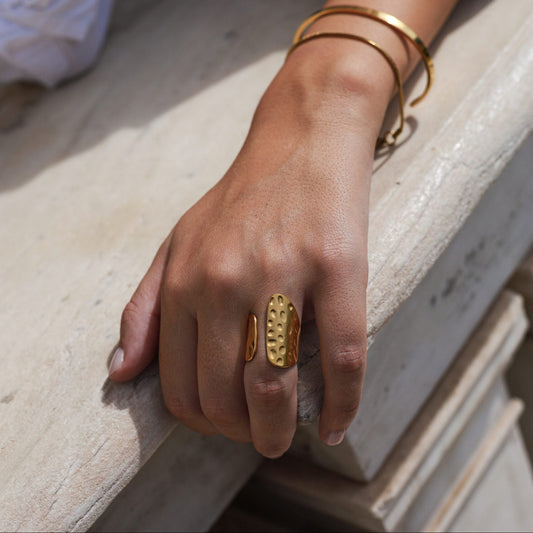Hand wearing gold rings and bracelets on a stone surface