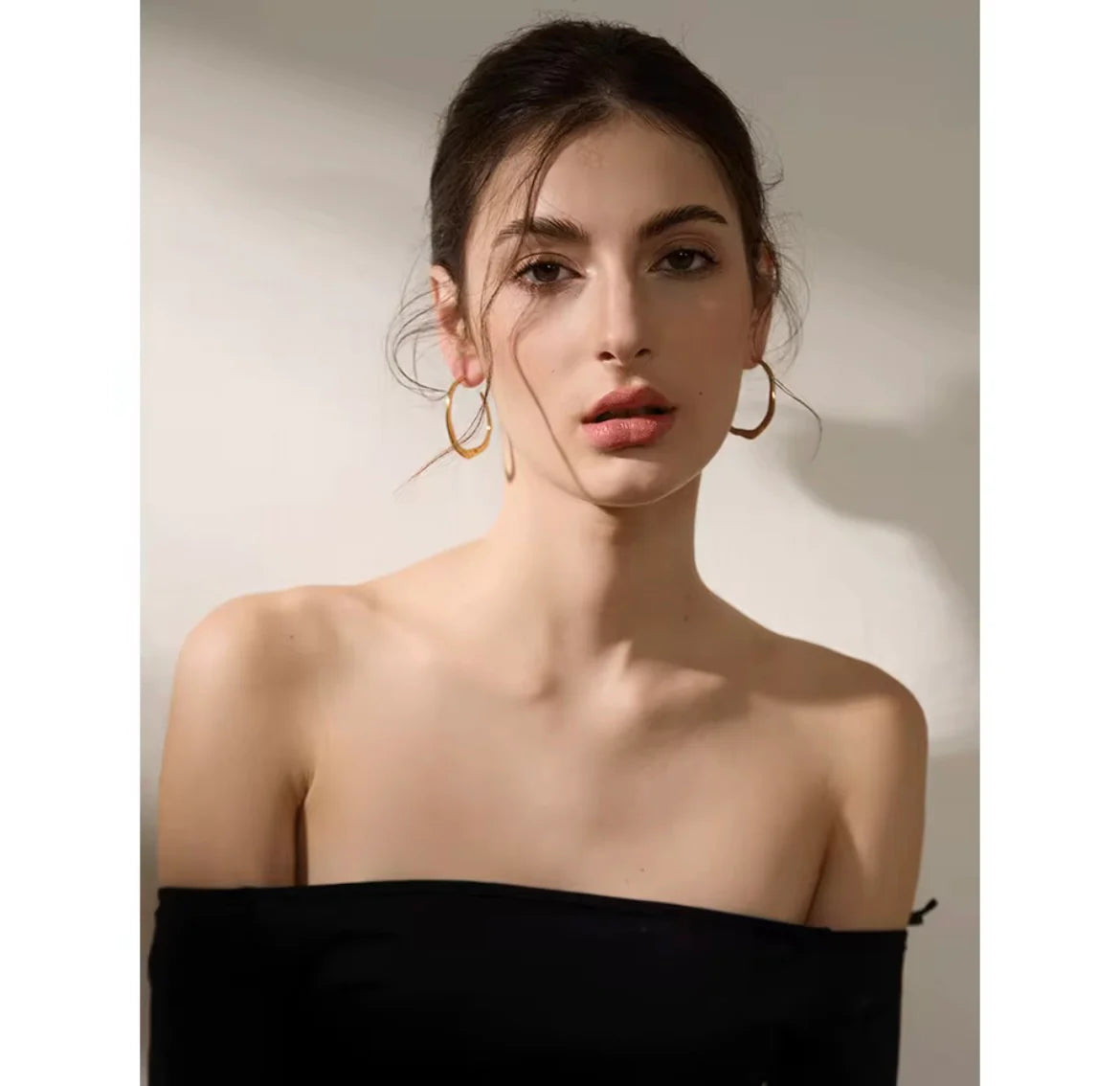 Woman wearing gold irregular hoop earrings against a neutral background