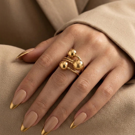 Gold ring on a hand with matching nail polish against a beige background
