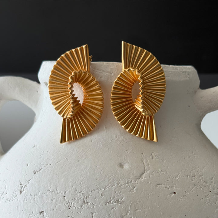 Gold earrings on a white stand with a dark background
