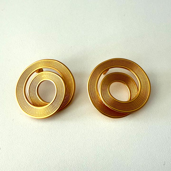 Pair of gold spiral earrings on a light beige background. Herae coil earrings
