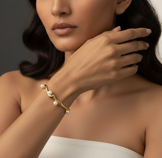Woman wearing a gold bracelet with pearls on a neutral background
