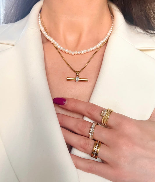 Close-up of a person wearing a gold necklace, pearl bracelet, and multiple rings on a white background