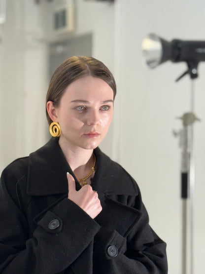 Person wearing a black coat with a coil earring from herae