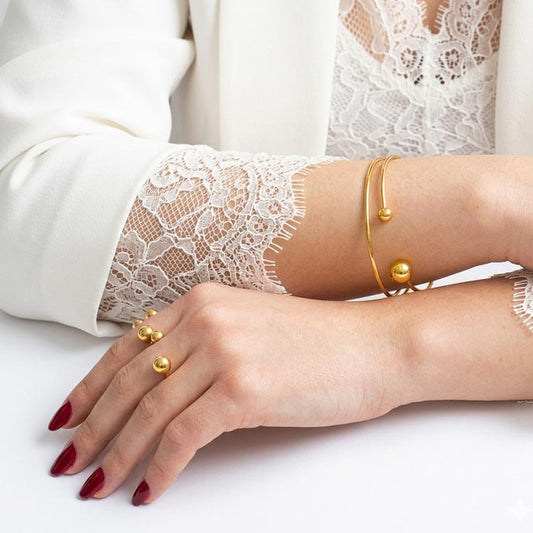 Herae 18K Ring and bangle set. Close-up of a person's hand wearing gold rings and bracelets on a white background