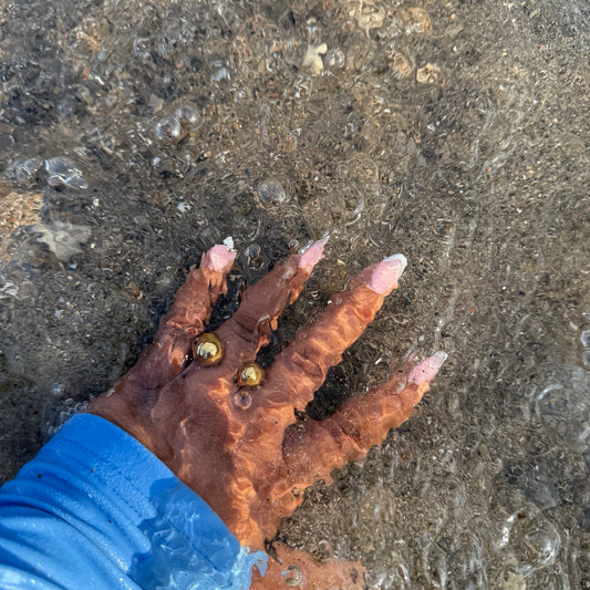 Hand with textured surface holding a small object against a wet sand background
