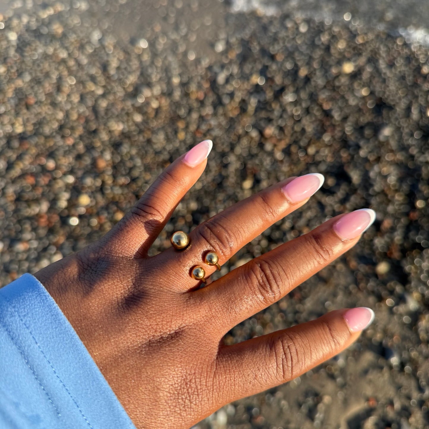 Hand with pink nail polish on a sandy background