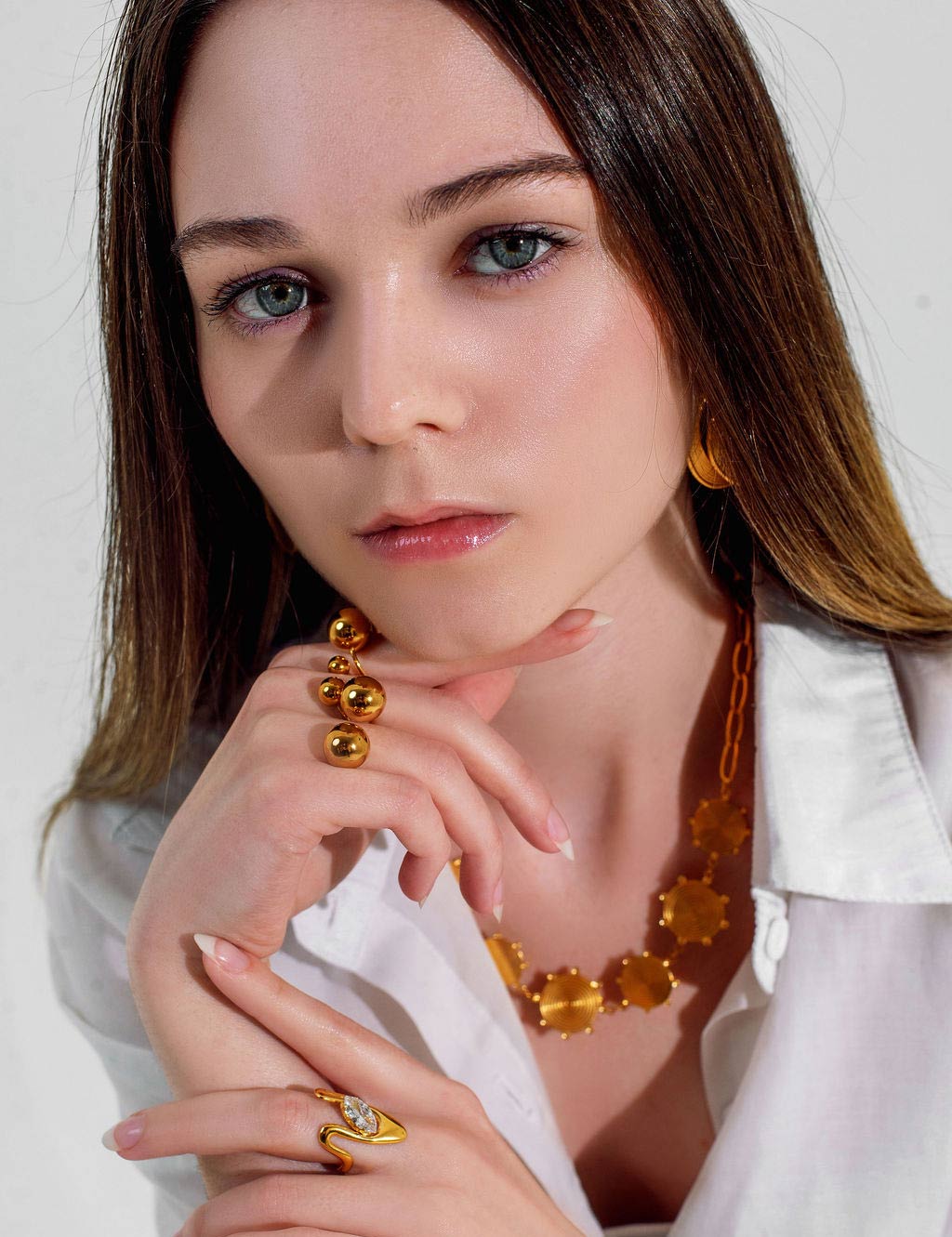 Woman wearing 18K gold jewelry including earrings, necklace, and ring on a white background