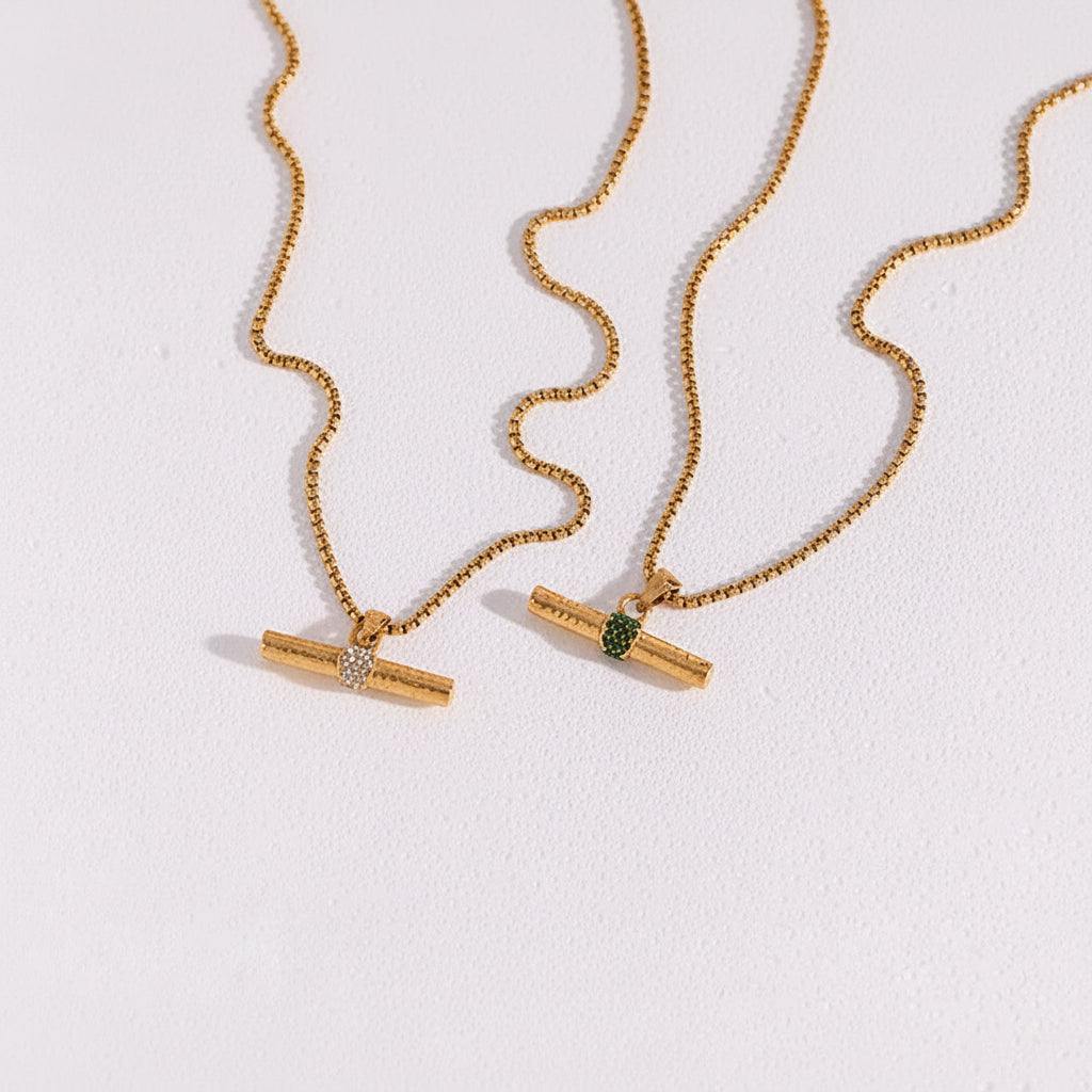 Two gold necklaces with pendant attachments on a textured white surface