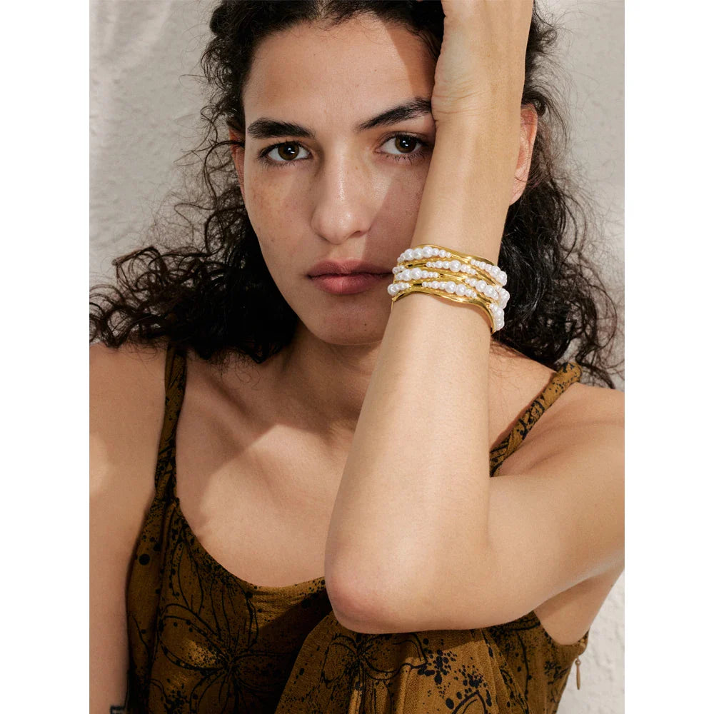 HERAW BABE wearing gold and pearl bracelets on a neutral background
