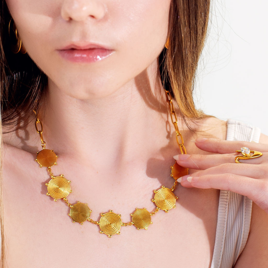 Woman wearing a gold necklace with circular designs, close-up of the necklace.
