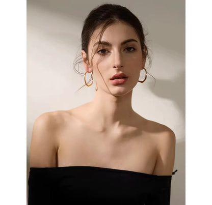 Woman wearing gold irregular  hoop earrings against a neutral background