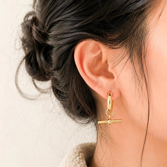 herae stainless steel Gold hoop earring with a small pendant worn by a person with dark hair.