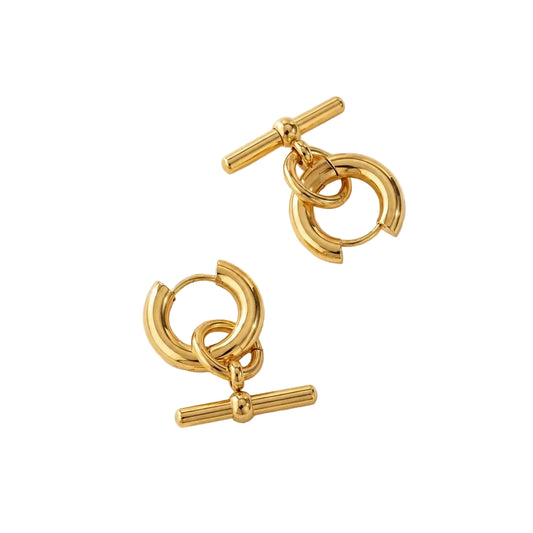 Pair of herae t-bar gold hoop earrings with a bar design on a beige background