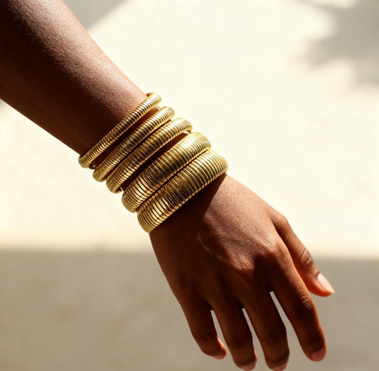 Hand wearing multiple gold rib bangles on a neutral background