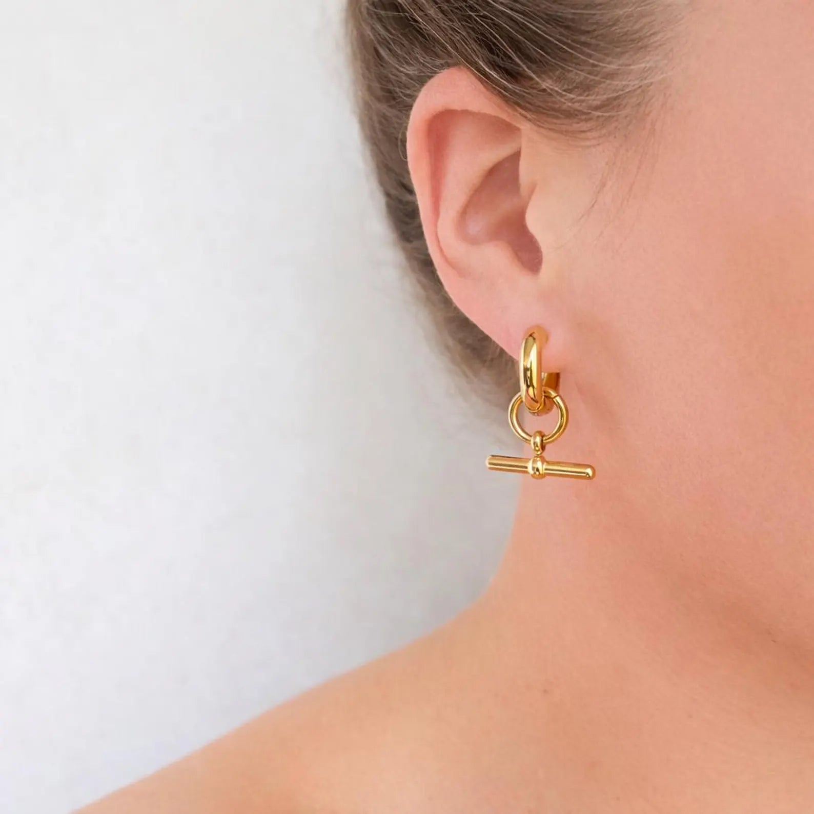 stainless steel t-bar Gold earring worn by a person on a white background
