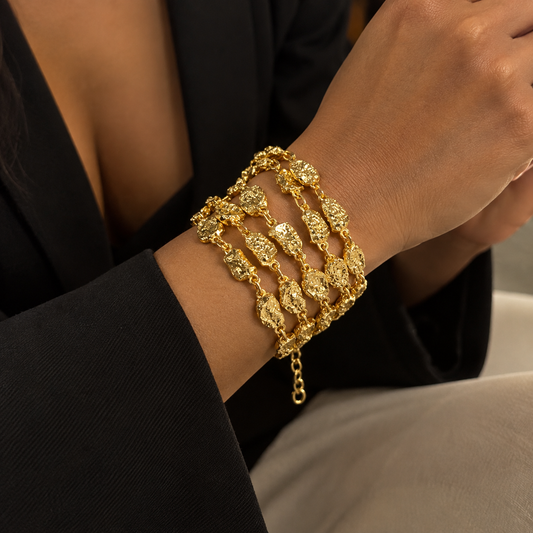 A close-up of a person's wrist wearing a stack of textured gold chain bracelets, paired with a black blazer.