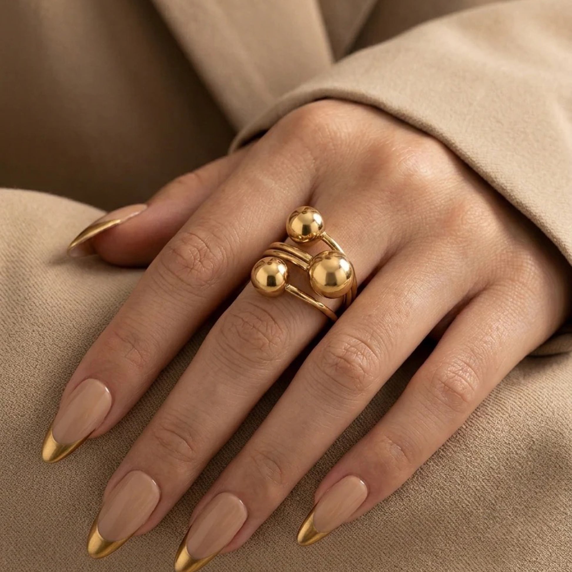 Gold ring on a hand with matching nail polish against a beige background