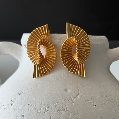 Gold earrings on a white stand with a dark background