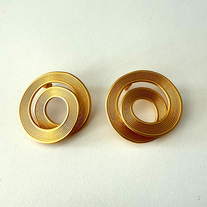 Pair of gold spiral earrings on a light beige background. Herae coil earrings