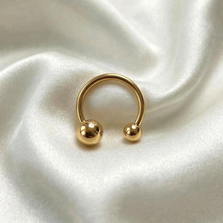 Gold hoop earring with two spherical ends on a white satin background