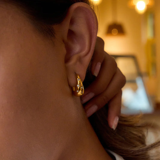 Close-up of a woman wearing a gold  gaze hoops earring from Herae