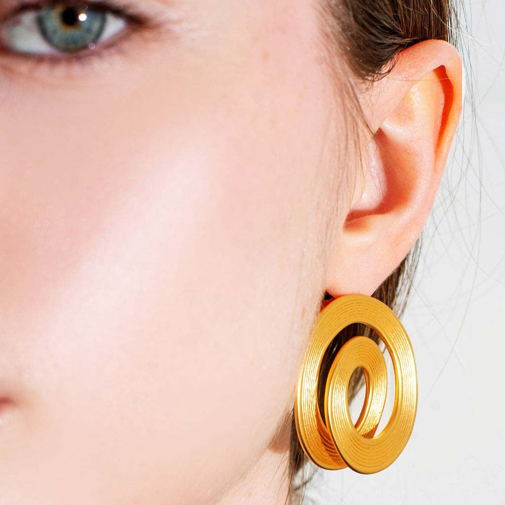 Gold hoop earrings worn by a model for herae jewelry with a neutral background