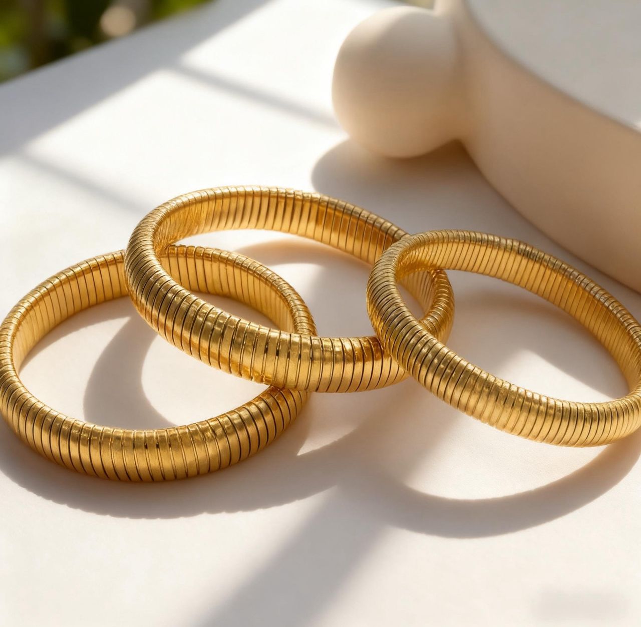 Three gold bangles on a light surface with a blurred background
