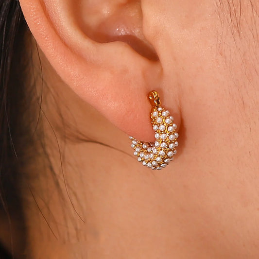 Gold and pearl hoop earring worn on an ear