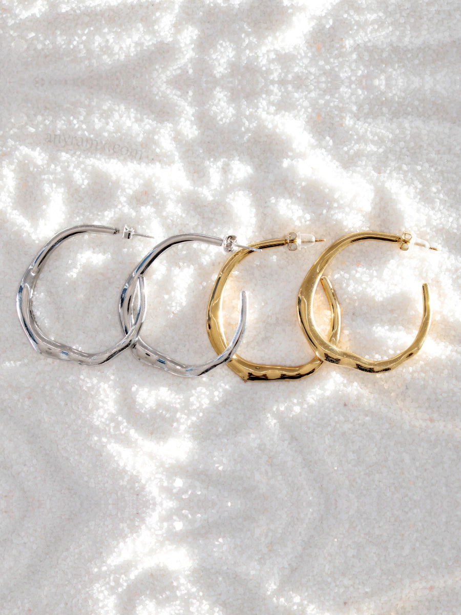 Two pairs of hoop earrings, one silver and one gold, on a sparkling white surface.