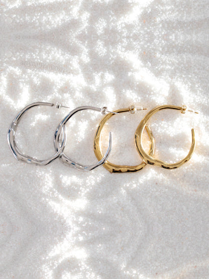 Two pairs of hoop earrings, one silver and one gold, on a sparkling white surface.