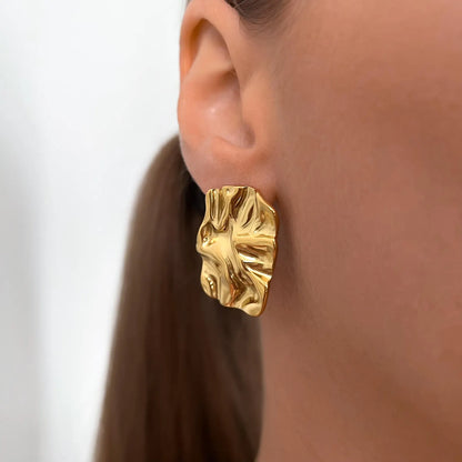 A close-up of a model's ear wearing a textured, organic-shaped gold earring.